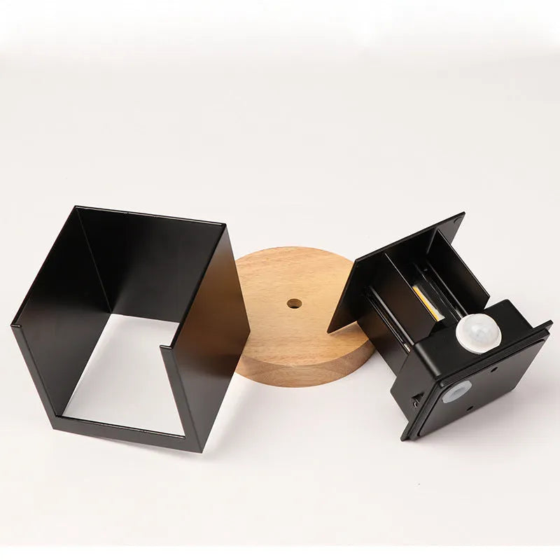Square black aluminium wall lamp with 360-degree light output mounted on a corridor wall.