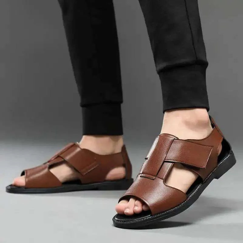 Men's black leather Roman sandals with open toe and non-slip rubber sole on a sandy beach.