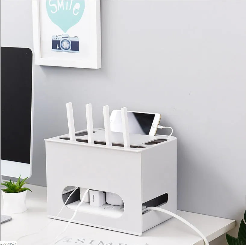 White plastic wireless router storage box with cable slots on a desk next to a router.