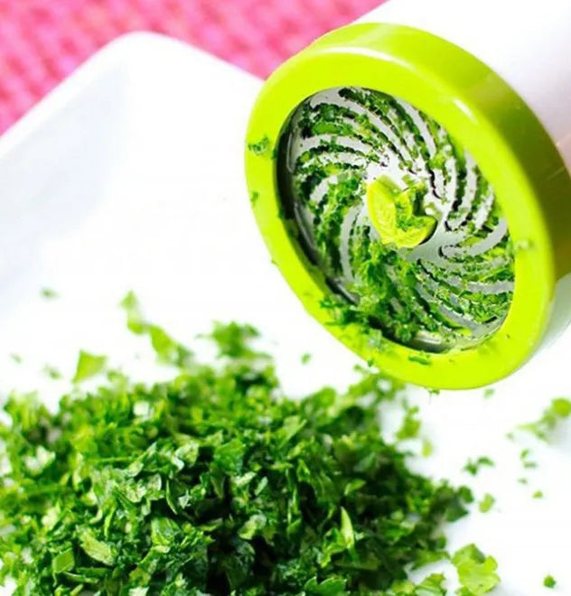 White and grey manual herb grinder with stainless steel blades and removable top on a kitchen counter.