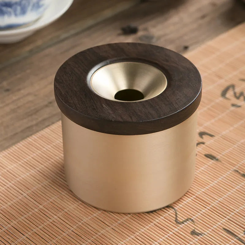 Brass-coloured copper ashtray with a wooden lid on a tabletop.