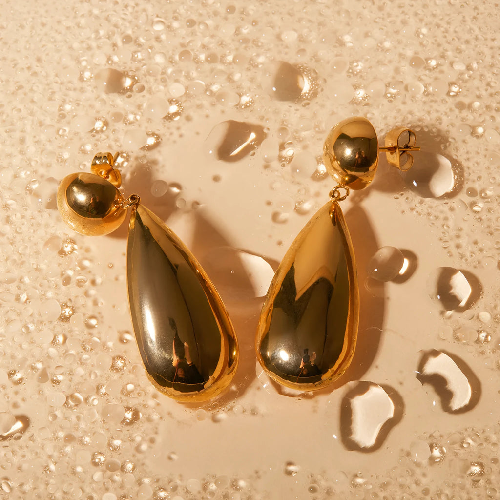 A pair of gold-coloured stainless steel earrings with a geometric water drop and hemisphere pendant design.