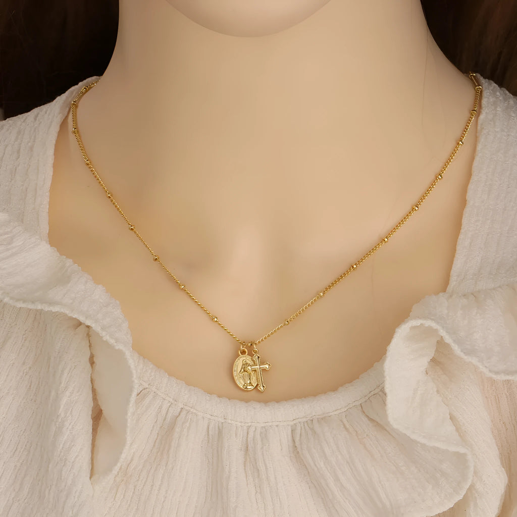 Gold geometric cross pendant necklace with Virgin Mary centre on a model.
