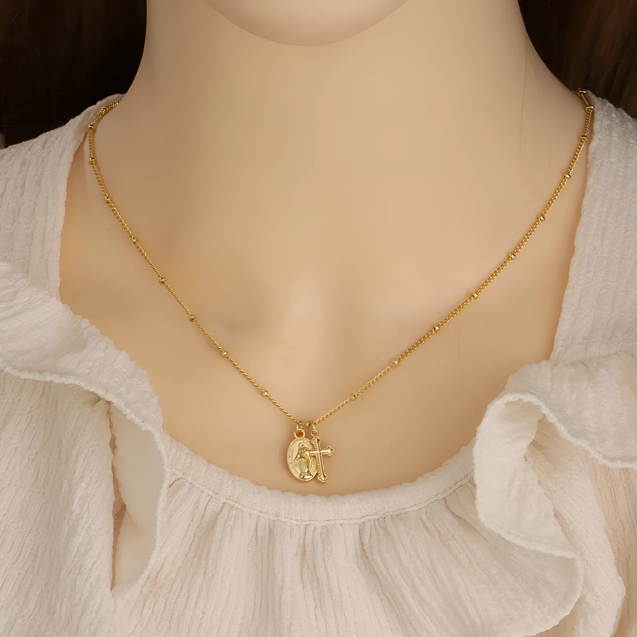 Gold geometric cross pendant necklace with Virgin Mary centre on a model.