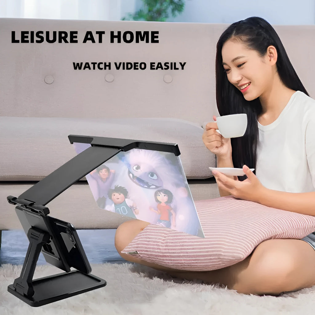 Black detachable mobile phone screen magnifier and holder set up on a desk, showing a phone displaying a magnified movie scene.