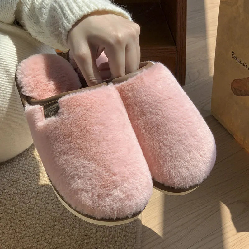 A pair of solid-colour plush winter slippers with a non-slip PVC sole on a wooden floor.