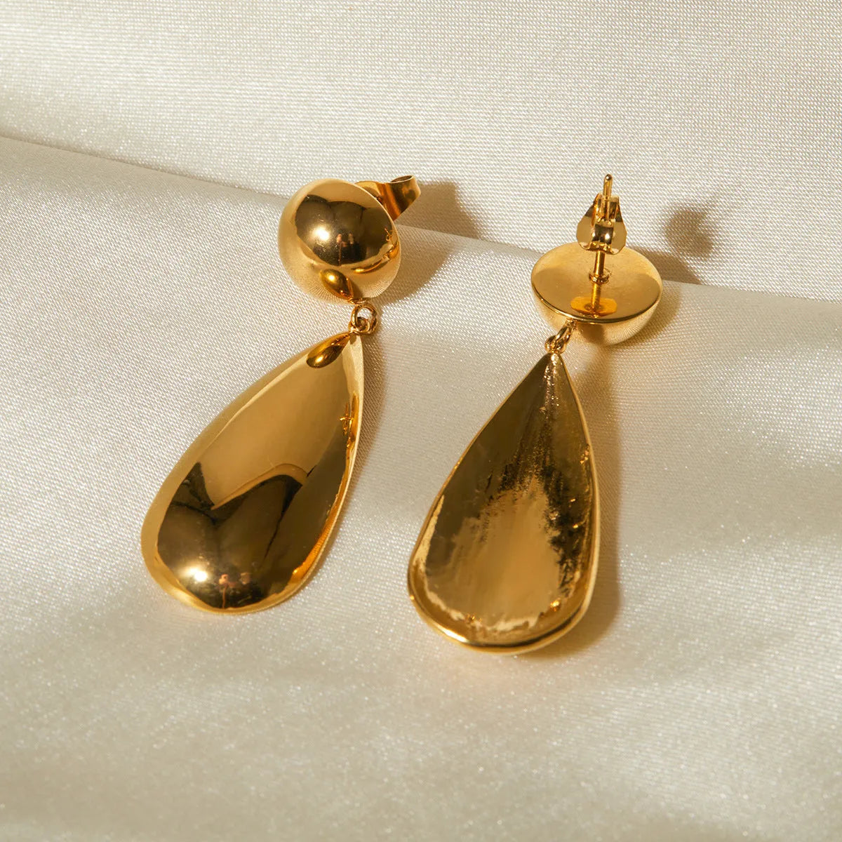 A pair of gold-coloured stainless steel earrings with a geometric water drop and hemisphere pendant design.