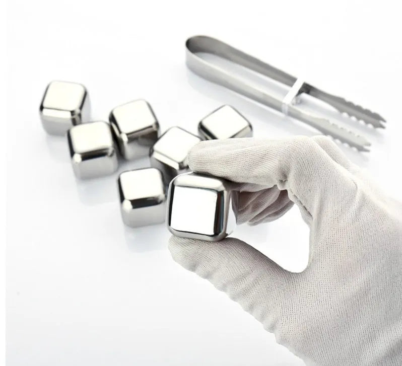 Set of stainless steel reusable whiskey stones in various shapes with metal tongs on a wooden surface.
