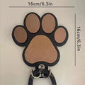 Black wooden wall hook with raised paw print design against a white wall.