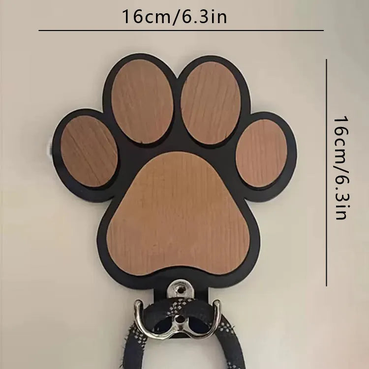 Black wooden wall hook with raised paw print design against a white wall.