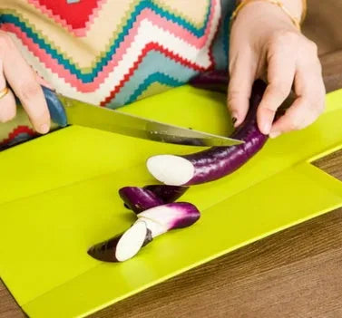 Green folding plastic cutting board with non-slip texture and hanging hole on kitchen countertop