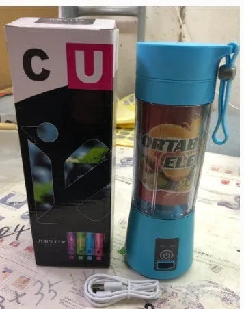 Mini USB electric fruit juicer with pink 400ml cup and stainless steel blades on a table.