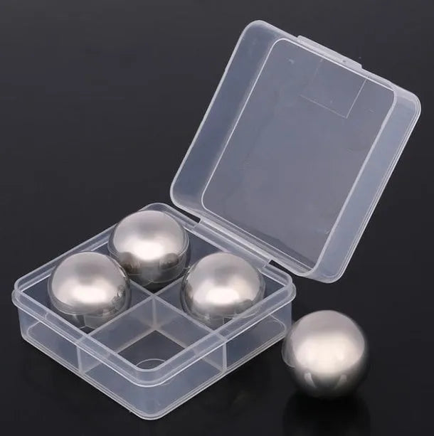 Set of stainless steel reusable whiskey stones in various shapes with metal tongs on a wooden surface.
