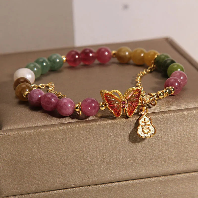 Close-up of an agate butterfly bracelet with a tourmaline-coloured gourd charm on a model's wrist.