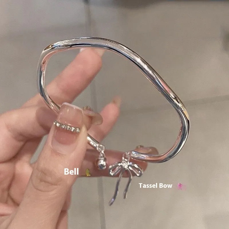 Silver adjustable bracelet with a bow charm on a wrist, showing the bell opening mechanism.