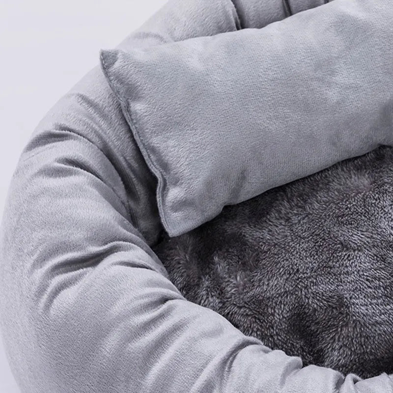 Grey round plush pet bed with pillow for small dogs and cats on a wood floor.