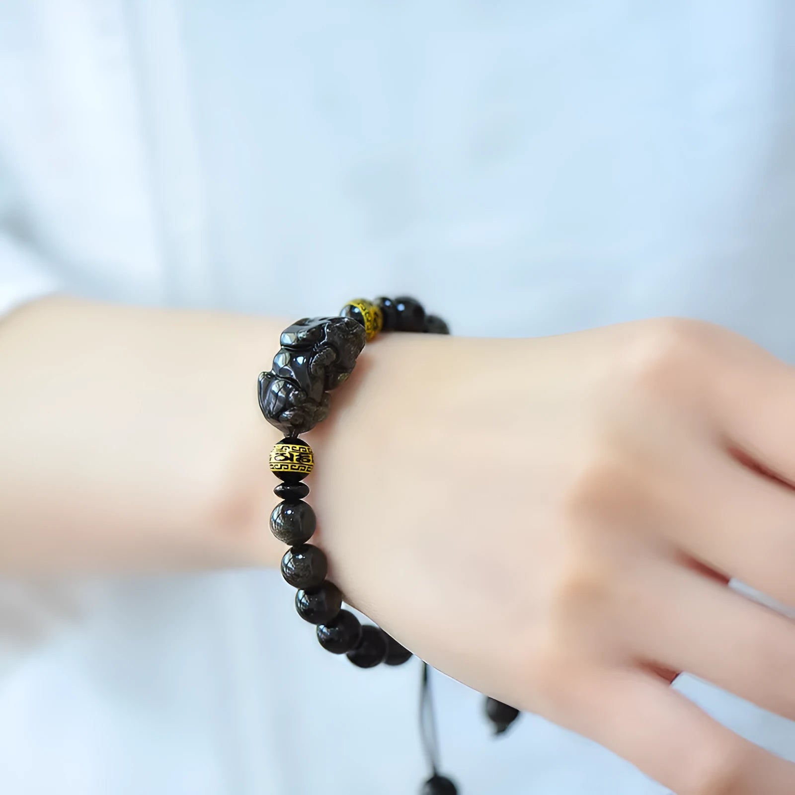 Hand-woven golden obsidian Pi Xiu bracelet with animal zodiac charm on wrist.