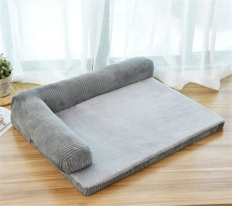 Grey corduroy pet sofa dog bed with bilateral bolsters and a non-slip cloth base on a wooden floor.
