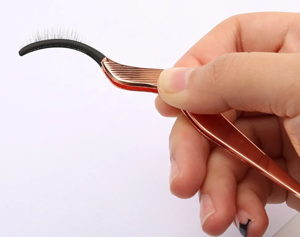 Rose gold metal false eyelash curler aid tool on plain background