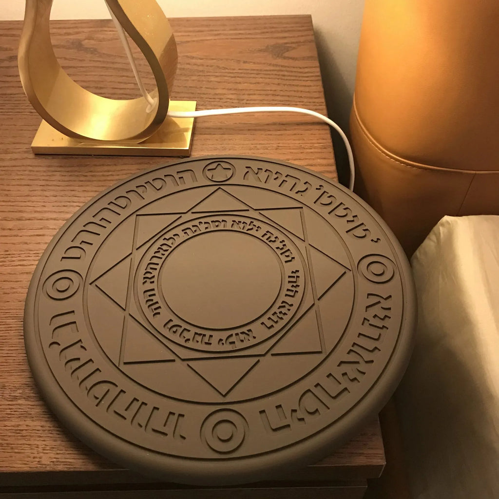 Square black wireless charging pad with glowing magic array pattern, charging a mobile phone.
