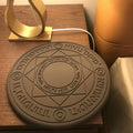 Square black wireless charging pad with glowing magic array pattern, charging a mobile phone.