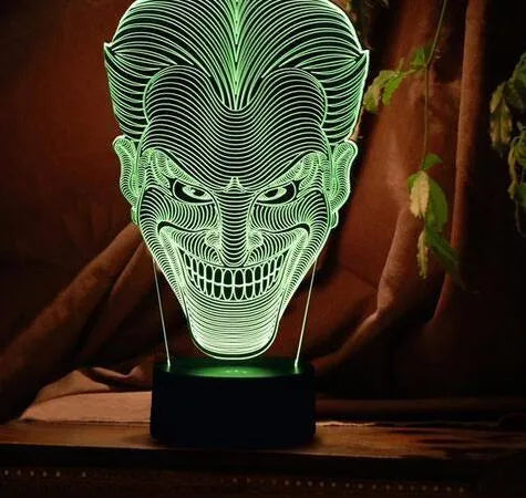 A 3D LED table lamp displaying multiple colours, with a remote control and USB cable on a desk.