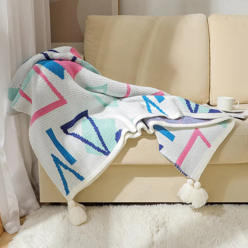 Bohemian style acrylic sofa cover blanket with tassel trim in a geometric pattern colour option.
