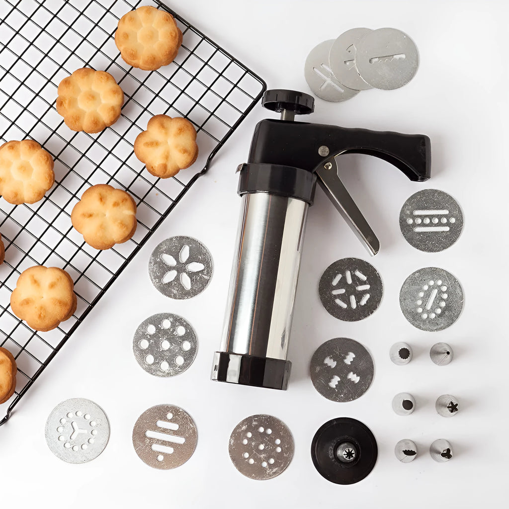 Stainless steel biscuit press gun with set of cookie moulds and piping nozzles on baking tray