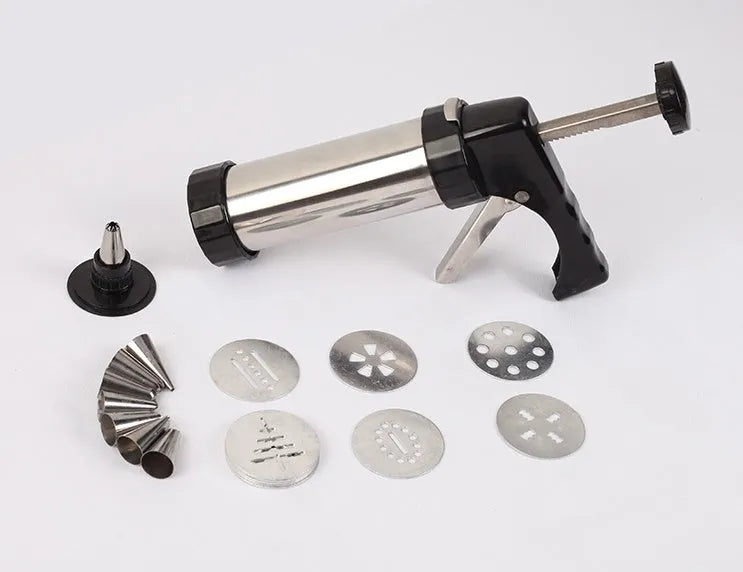 Stainless steel biscuit press gun with set of cookie moulds and piping nozzles on baking tray