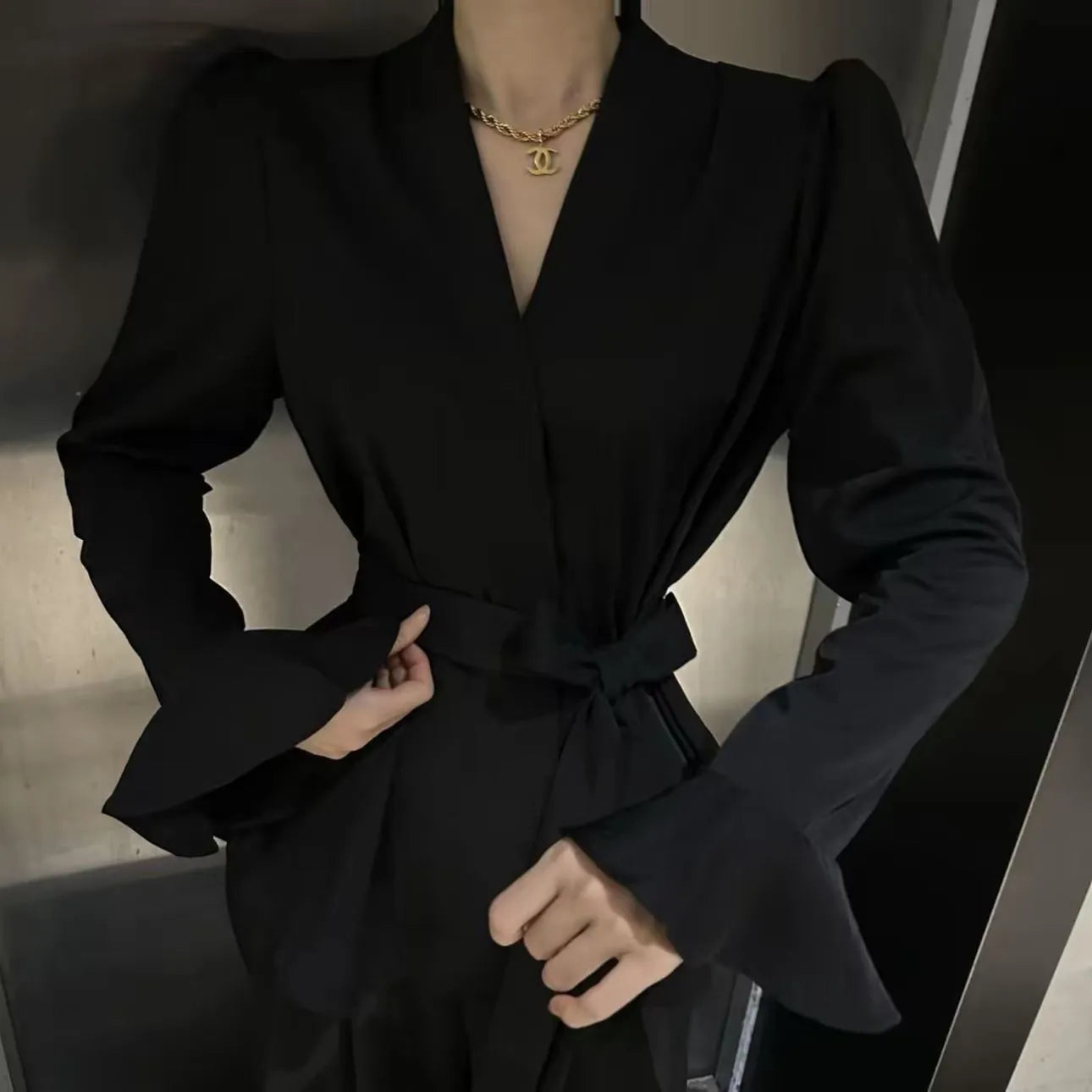 Women's black shirt with an irregular collar and long bell sleeves on a model.