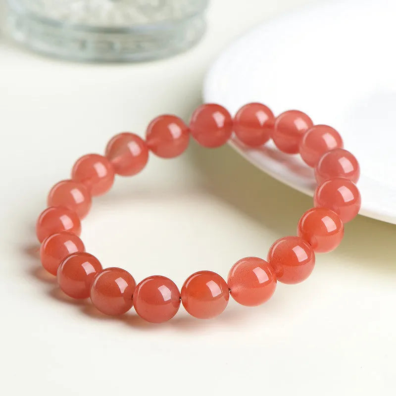 A close-up of a polished cherry red agate bead bracelet on a wrist.