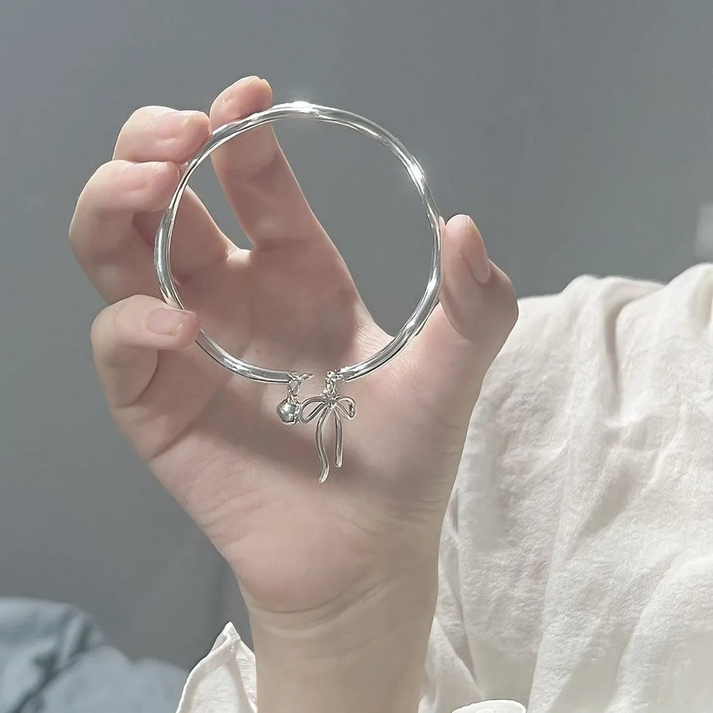Silver adjustable bracelet with a bow charm on a wrist, showing the bell opening mechanism.