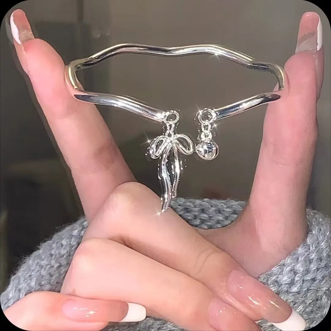 Silver adjustable bracelet with a bow charm on a wrist, showing the bell opening mechanism.
