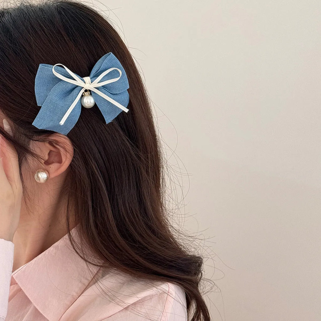 A women's hair clip barrette with a soft blue cloth bow and lace decoration on a plastic clip.