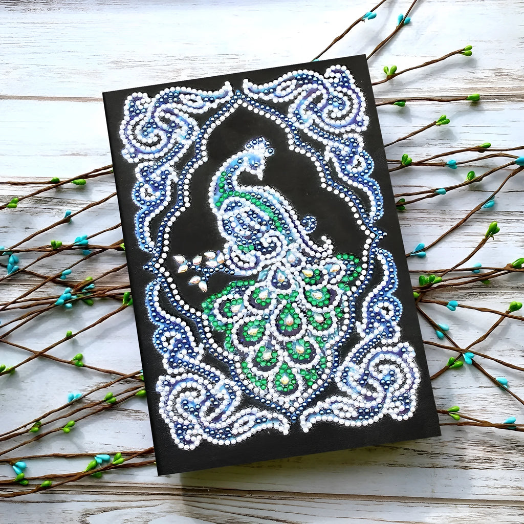 Black A5 diamond painting notebook with peacock design, open to show shaped and bright drills on page.
