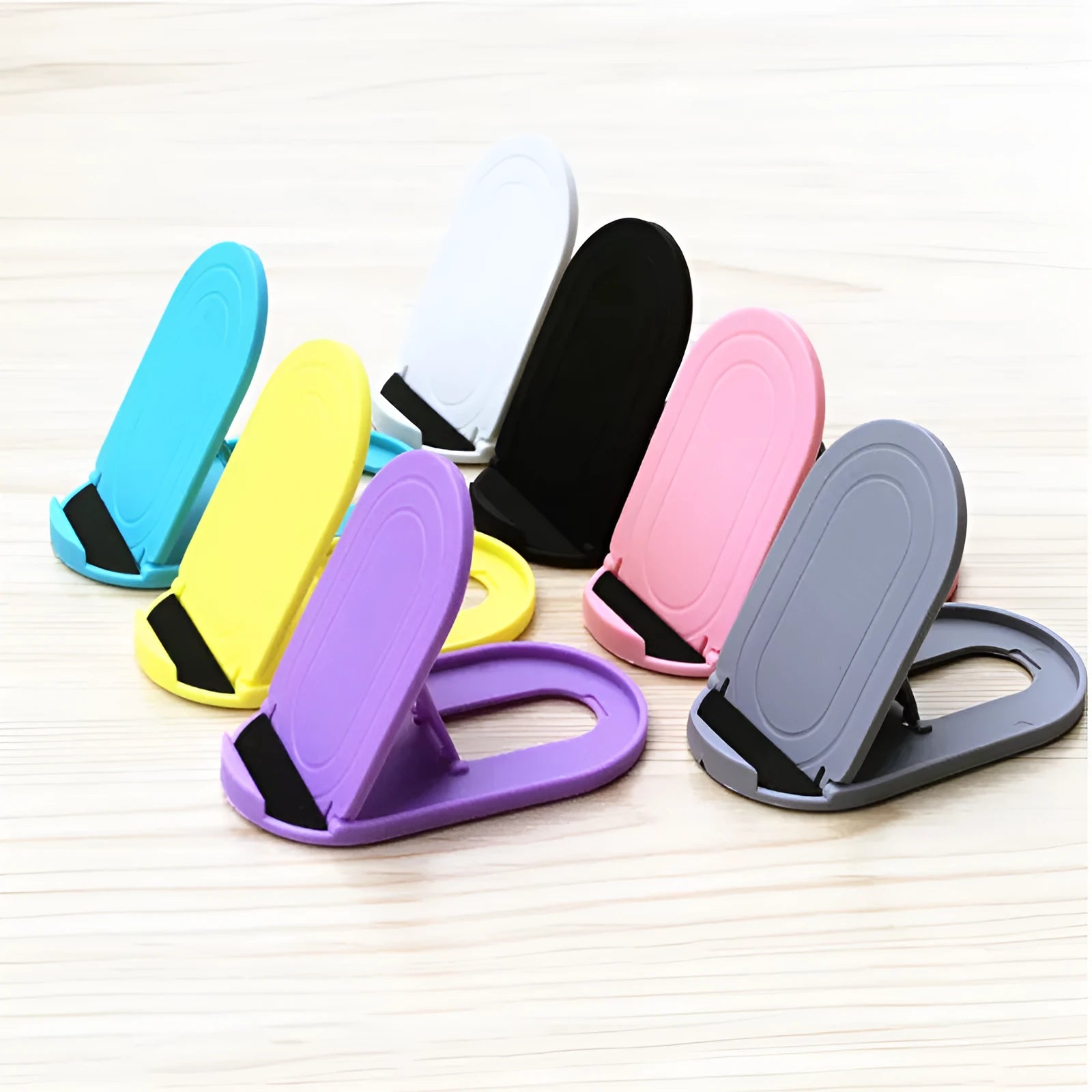 Plastic lazy bracket mobile phone stand in six colour options holding a smartphone on a wooden desk.
