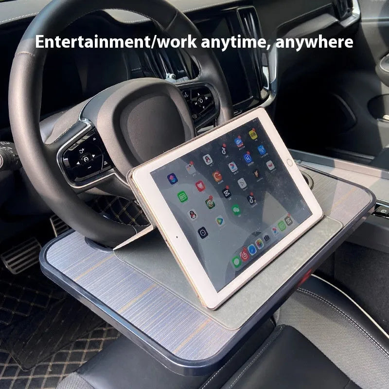 Black foldable car steering wheel laptop stand with a drink cup holder on a table.