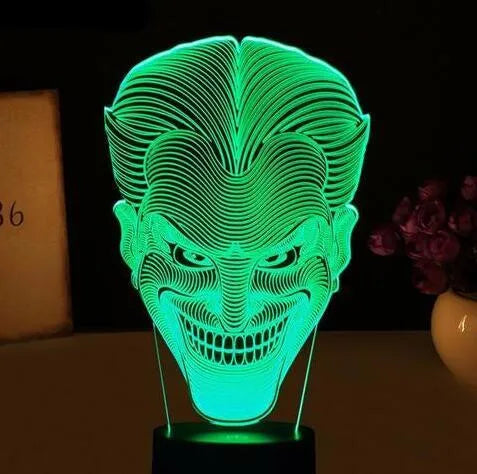 A 3D LED table lamp displaying multiple colours, with a remote control and USB cable on a desk.