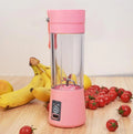 Mini USB electric fruit juicer with pink 400ml cup and stainless steel blades on a table.