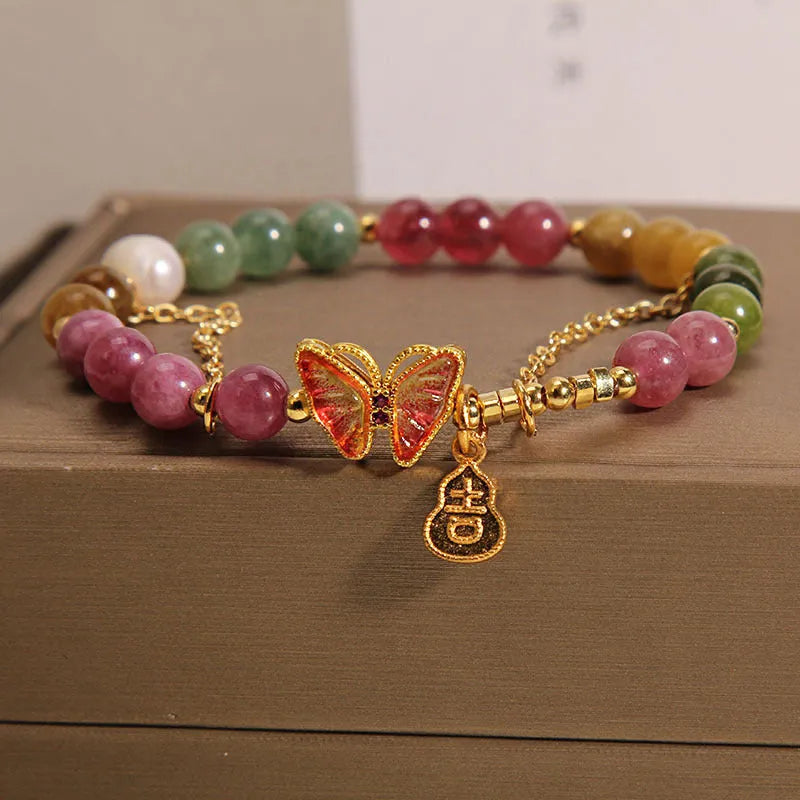 Close-up of an agate butterfly bracelet with a tourmaline-coloured gourd charm on a model's wrist.