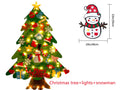 Green DIY felt Christmas tree with fairy lights and ornaments on a white wall with decorations attached