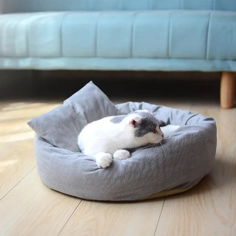 Grey round plush pet bed with pillow for small dogs and cats on a wood floor.