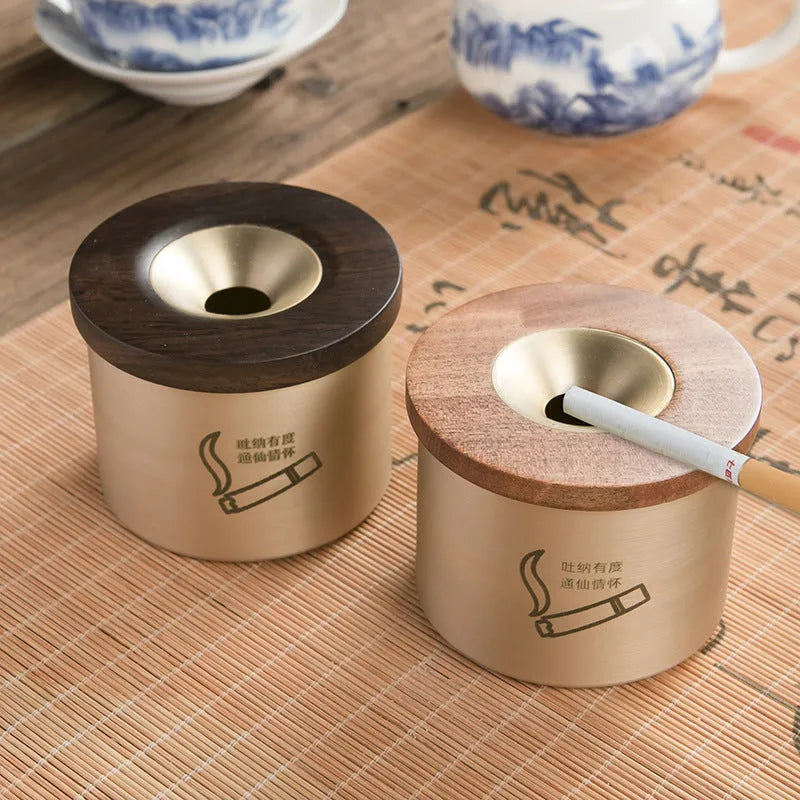 Brass-coloured copper ashtray with a wooden lid on a tabletop.
