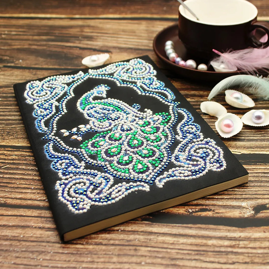 Black A5 diamond painting notebook with peacock design, open to show shaped and bright drills on page.