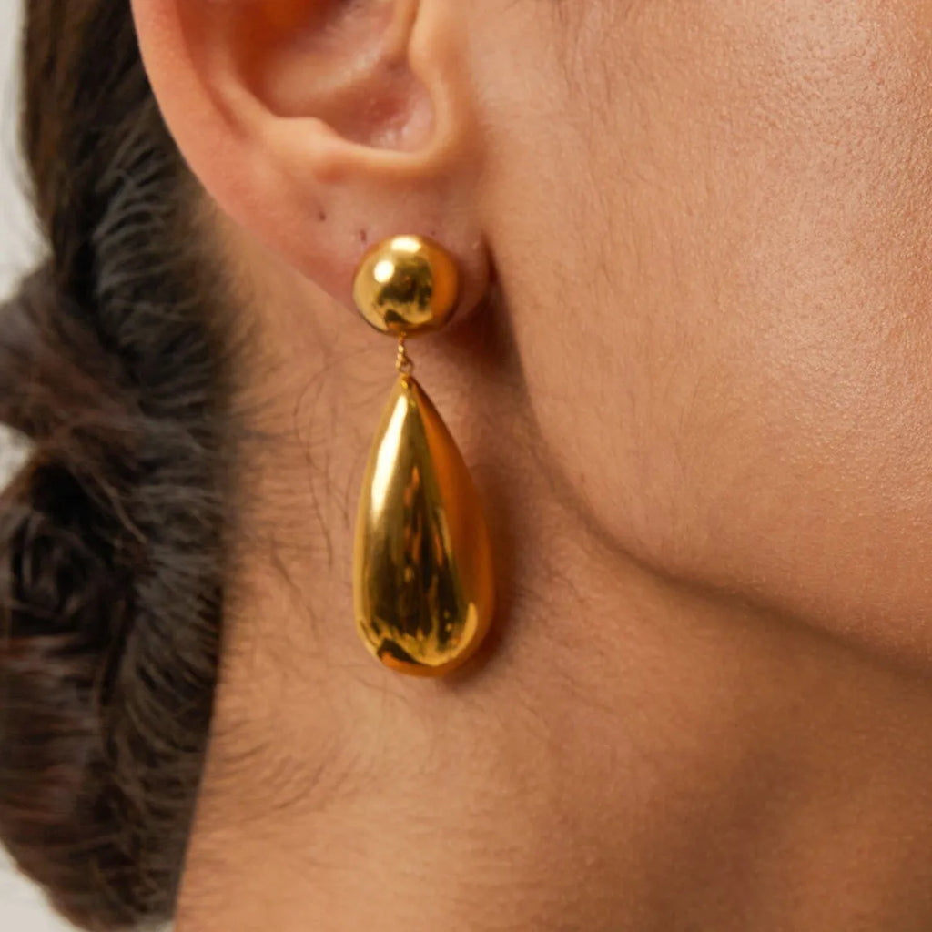 A pair of gold-coloured stainless steel earrings with a geometric water drop and hemisphere pendant design.