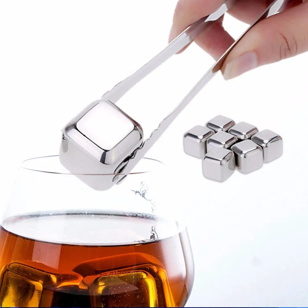 Set of stainless steel reusable whiskey stones in various shapes with metal tongs on a wooden surface.