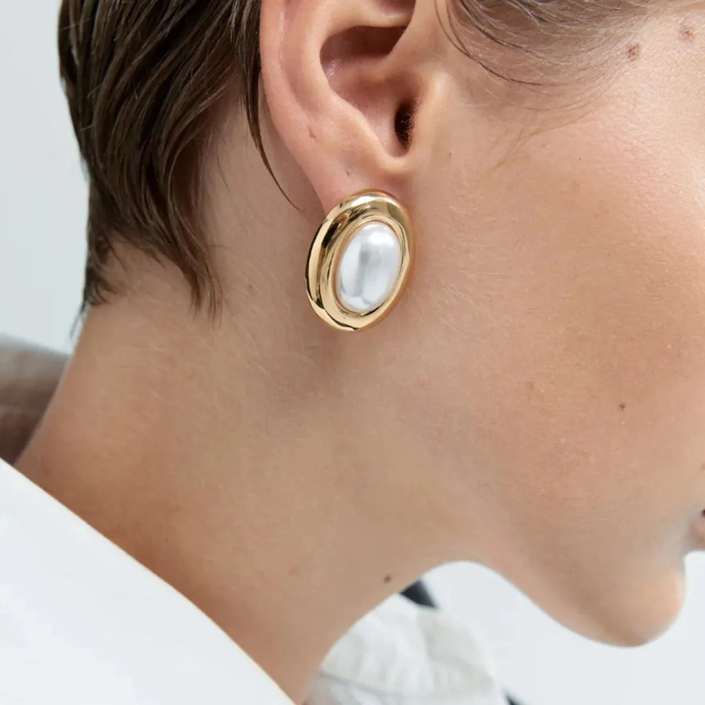 Small vintage-style pearl ear studs with a gold-tone finish on a stainless steel post.