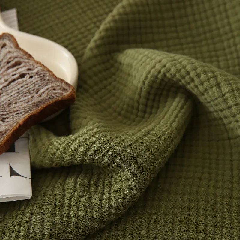 Four-layer gauze cotton blanket with tassel trim in avocado green, laid flat.