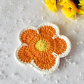 Set of five handmade woven flower placemats in blue, green, orange, pink, and purple colours on a wooden table.