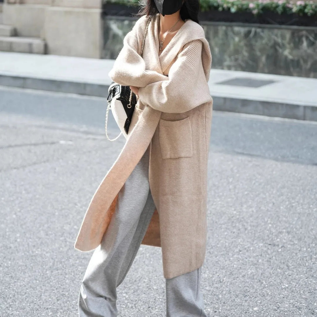 Long grey knitted hooded cardigan coat with long sleeves on a hanger.